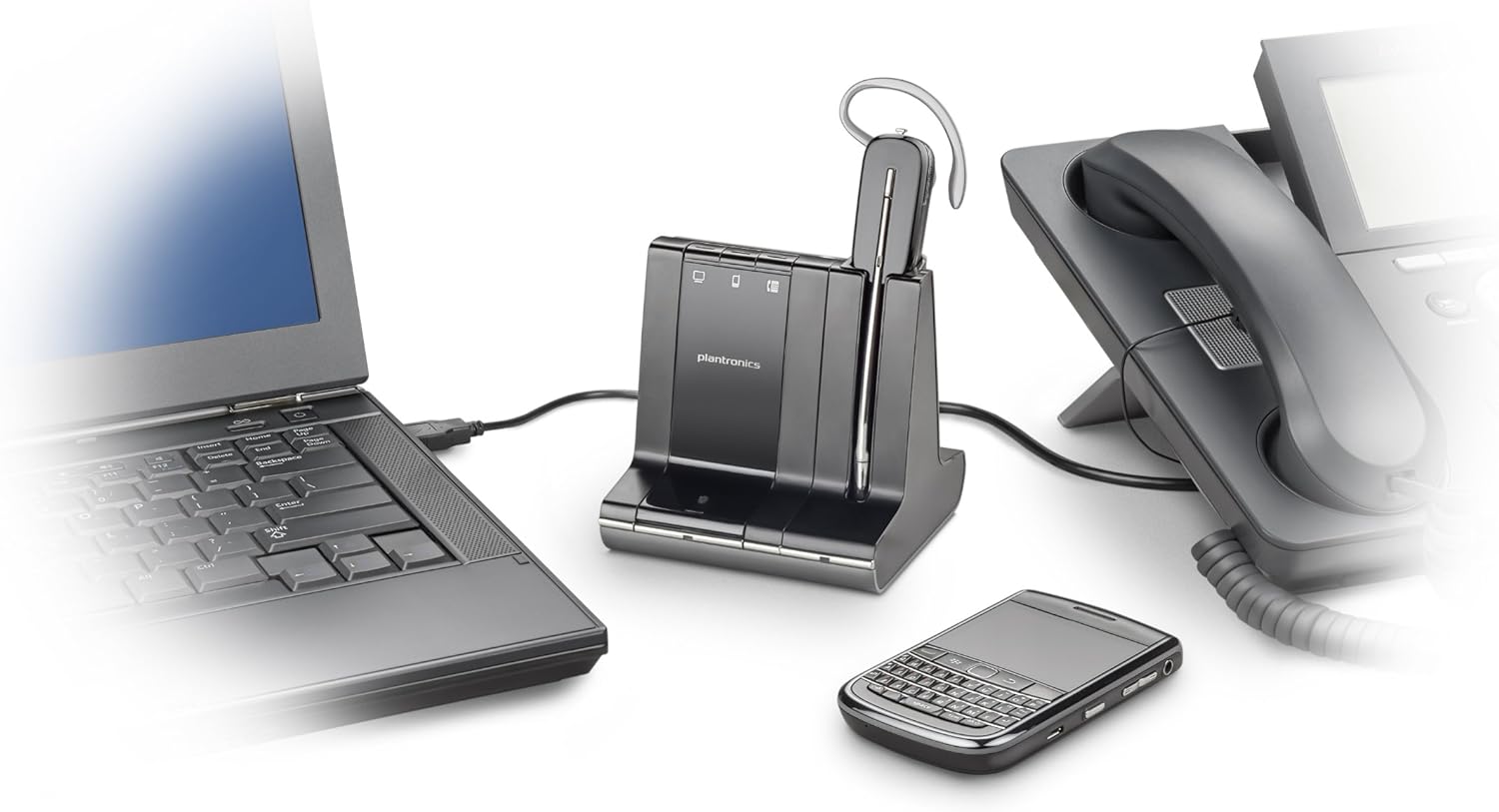 A desk setup featuring a laptop, a Poly Plantronics Savi W740 Wireless Headset System (83542-01) with noise-canceling mic and its charging base, a desktop phone, and a smartphone. The laptop is open, and all devices are positioned closely together, highlighting a workspace optimized for 3-way connectivity and productivity.