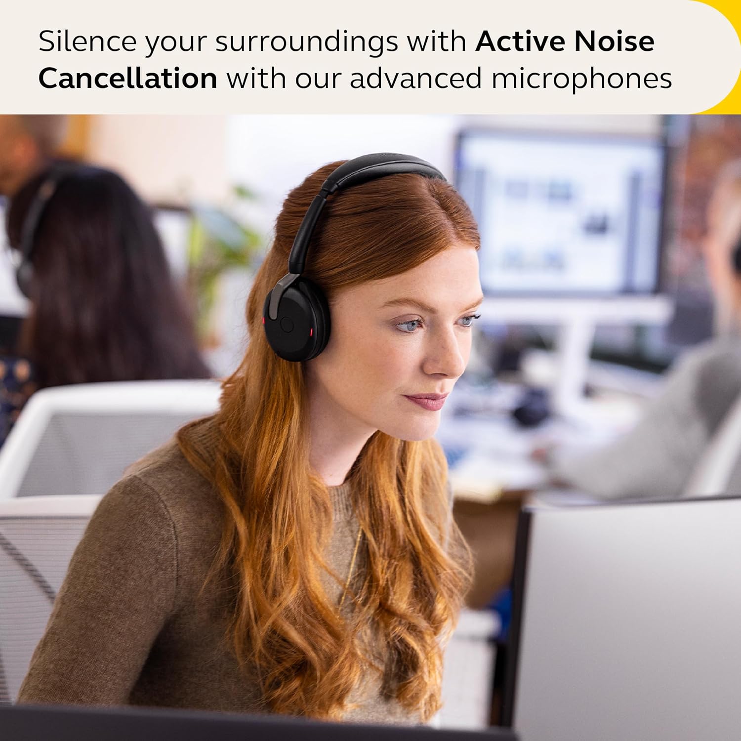 A woman with long red hair is wearing black headphones while sitting in an office environment. She is focused on her computer screen. The text above her reads, "Silence your surroundings with Hybrid ANC and advanced microphones found in the Jabra Evolve2 65 Flex Wireless Stereo Headset - Bluetooth, Noise-Cancelling ClearVoice Technology & Hybrid ANC - Works with All Leading UC Platforms Such As Zoom & Google Meet - Black by JABRA.