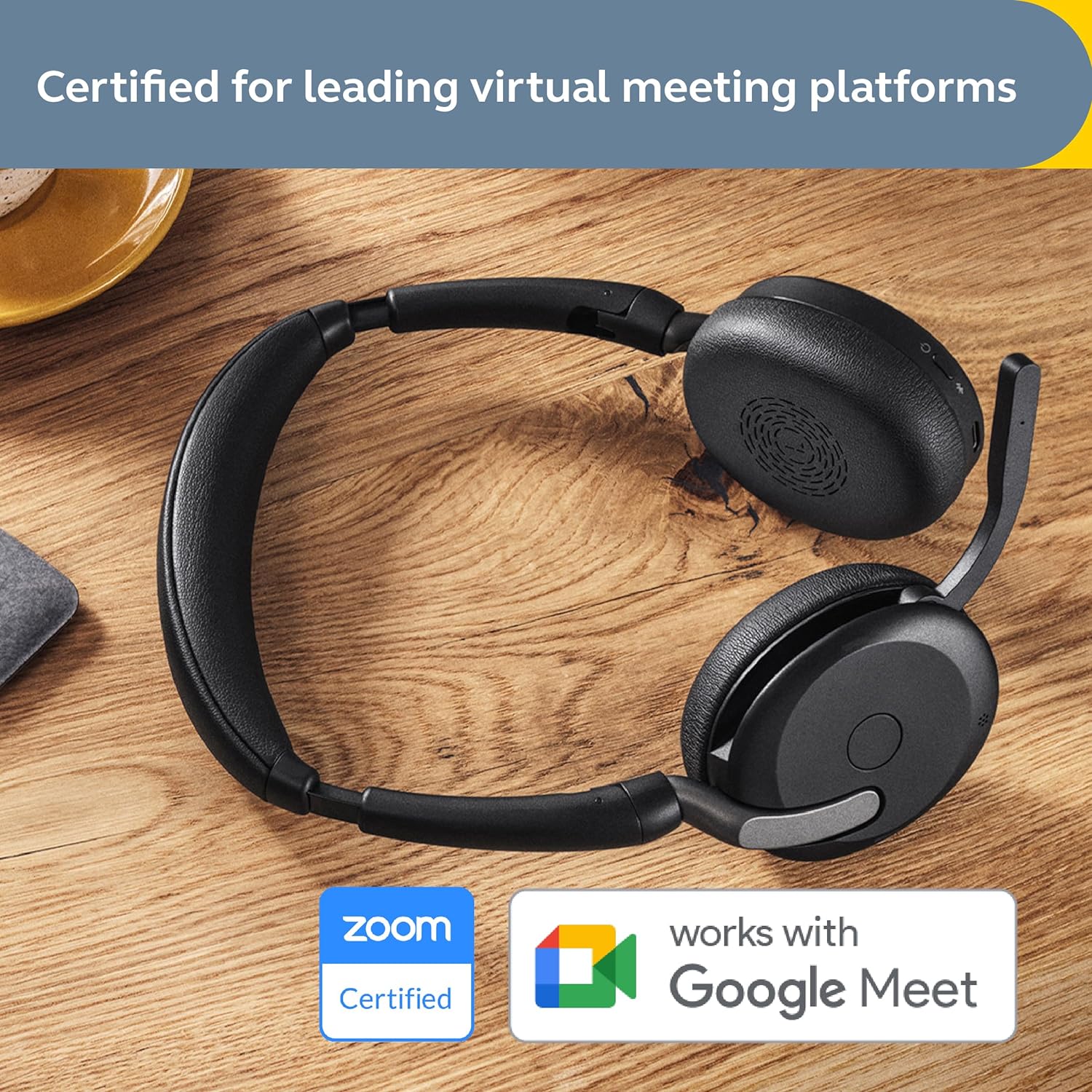 A black Jabra Evolve2 65 Flex Wireless Stereo Headset - Bluetooth, Noise-Cancelling ClearVoice Technology & Hybrid ANC - Works with All Leading UC Platforms Such As Zoom & Google Meet - Black is placed on a wooden surface. The top of the image displays the text "Certified for leading virtual meeting platforms." The bottom of the image shows the Zoom Certified logo and the Google Meet logo, indicating compatibility.